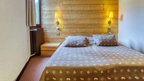 Een slaapkamer met een houten hoofdeinde, twee bedlampen, een bed met beddengoed met een patroon, en een raam met gordijnen.