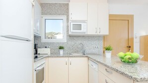 A modern kitchen with white cabinets, a granite countertop, a microwave, a sink, and a window with a view of the outdoors. - Santa Lucia by Interhome (Roses)
