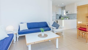 A modern living room with a blue sofa, white armchairs, a small white table, and a kitchen in the background. - Santa Lucia by Interhome (Roses)