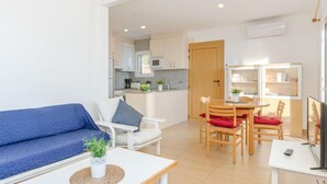 A modern living room with a blue sofa, a small table with a plant, and a dining area with wooden chairs and a table. - Santa Lucia by Interhome (Roses)