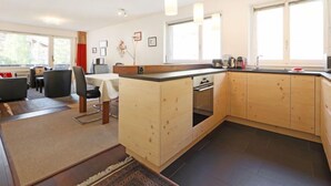 Una cocina moderna con armarios de madera, un comedor con mesa y sillas, y vistas al exterior a través de grandes ventanales.