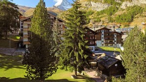 Un complejo turístico de montaña con edificios de madera, un telesilla y un pico montañoso destacado al fondo.