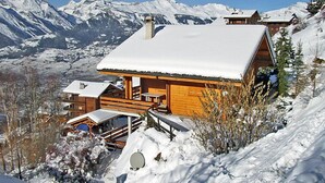 Eine Holzhütte mit verschneitem Dach, umgeben von Bergen und schneebedeckten Bäumen.