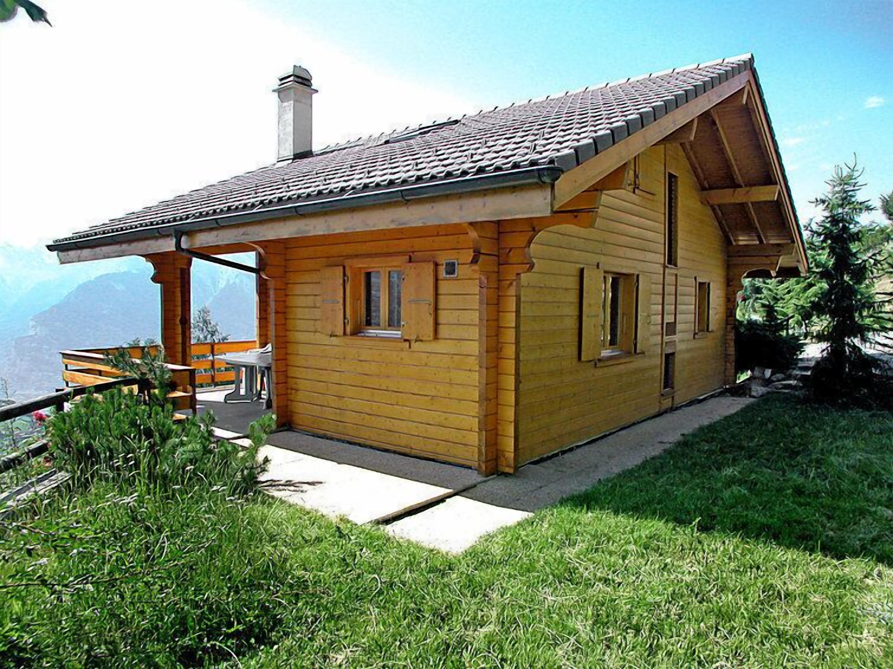 Een houten chalet met schuin dak, schoorsteen en een bankje ervoor.