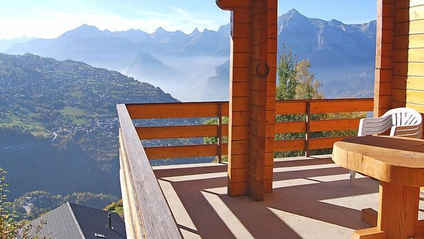 Eine Holzterrasse mit Tisch und Stühlen mit Blick auf eine Berglandschaft.