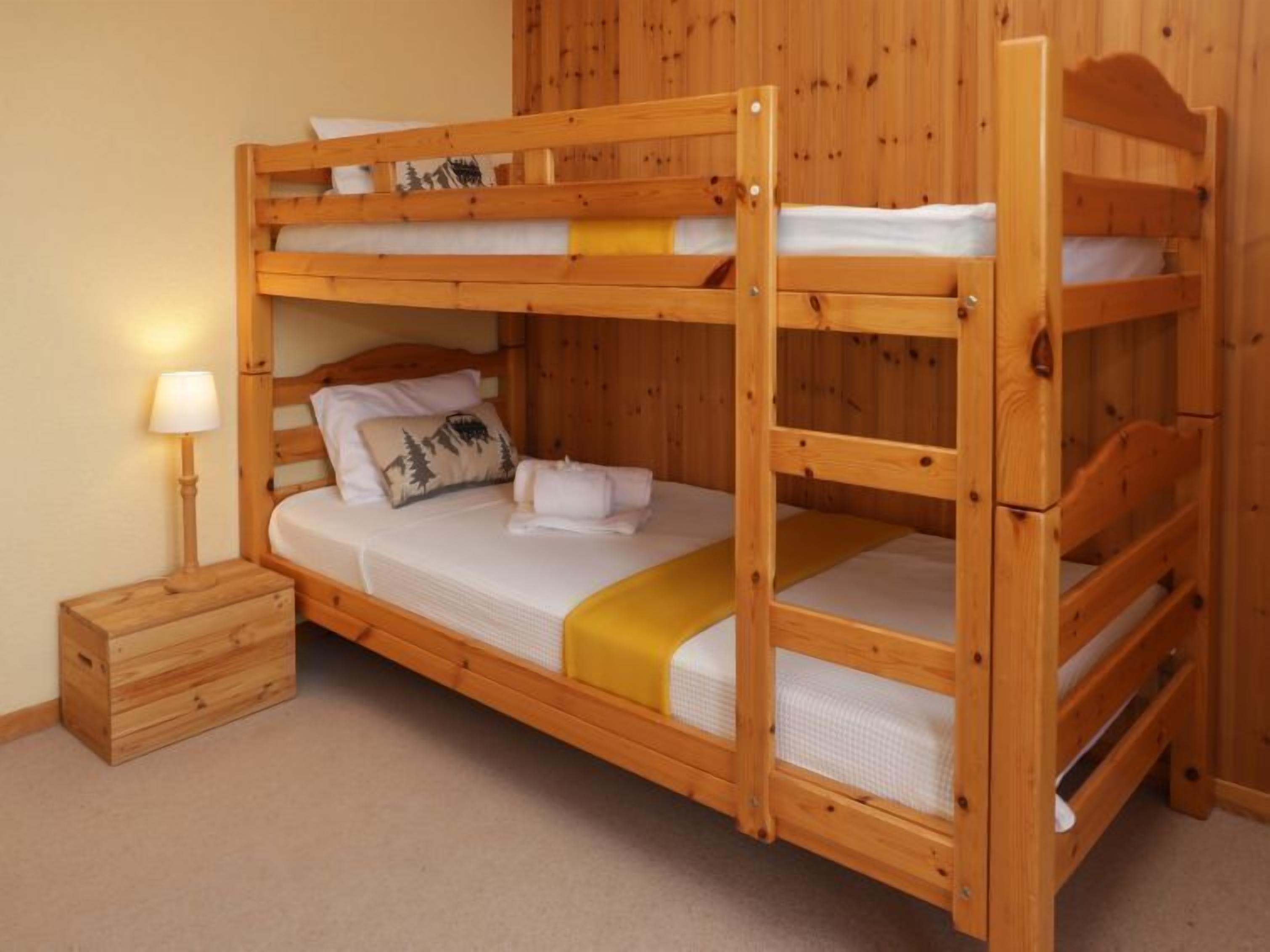 Une chambre avec un lit superposé aux finitions en bois, une table de chevet avec une lampe et une petite commode en bois.