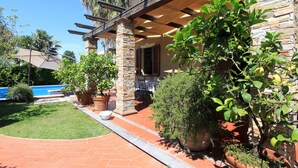 A house with a stone facade, a covered porch, and a swimming pool in the background.