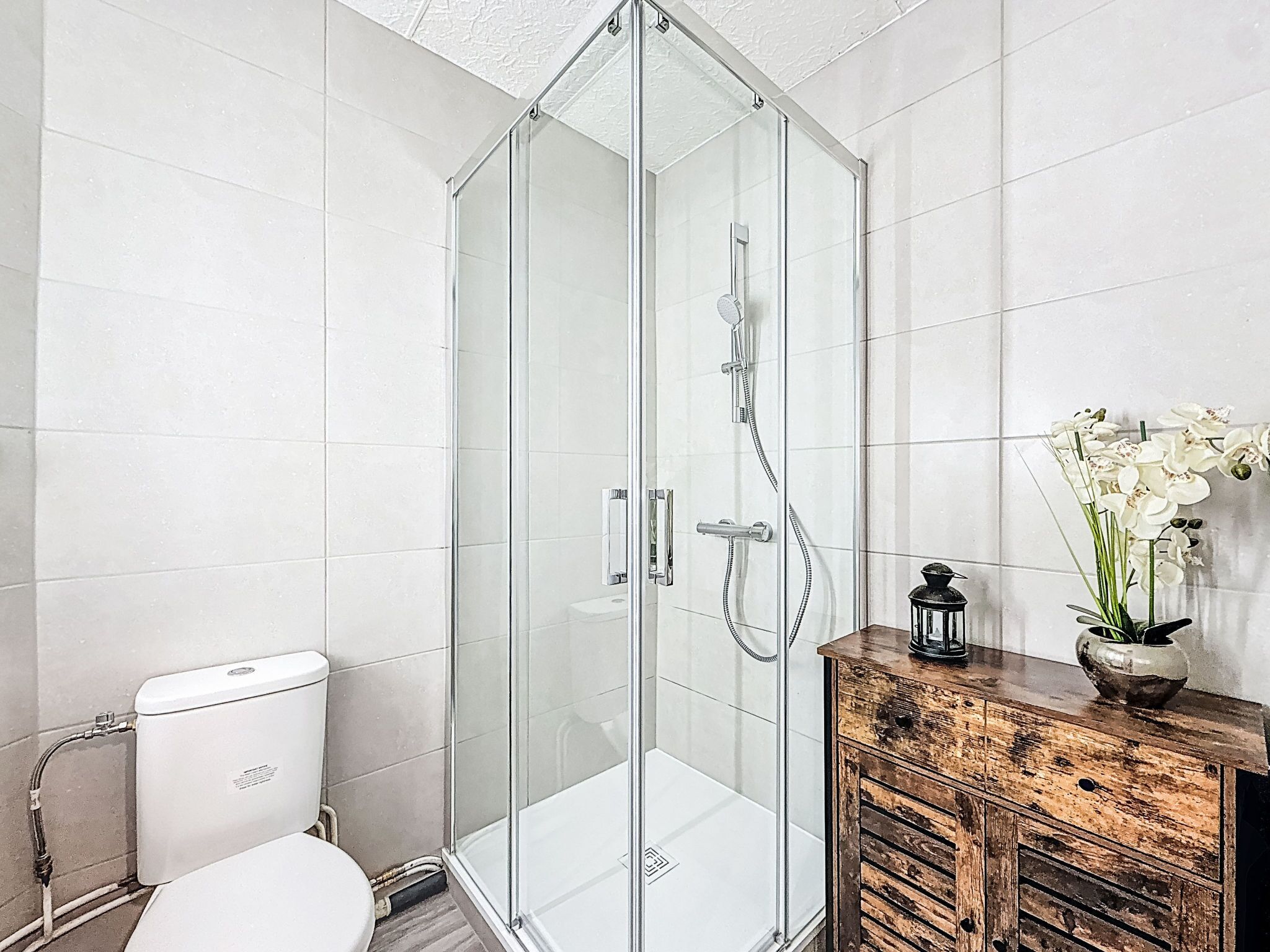 Une salle de bain moderne avec une douche à parois de verre, des toilettes et un meuble en bois sur lequel est posé un vase de fleurs.