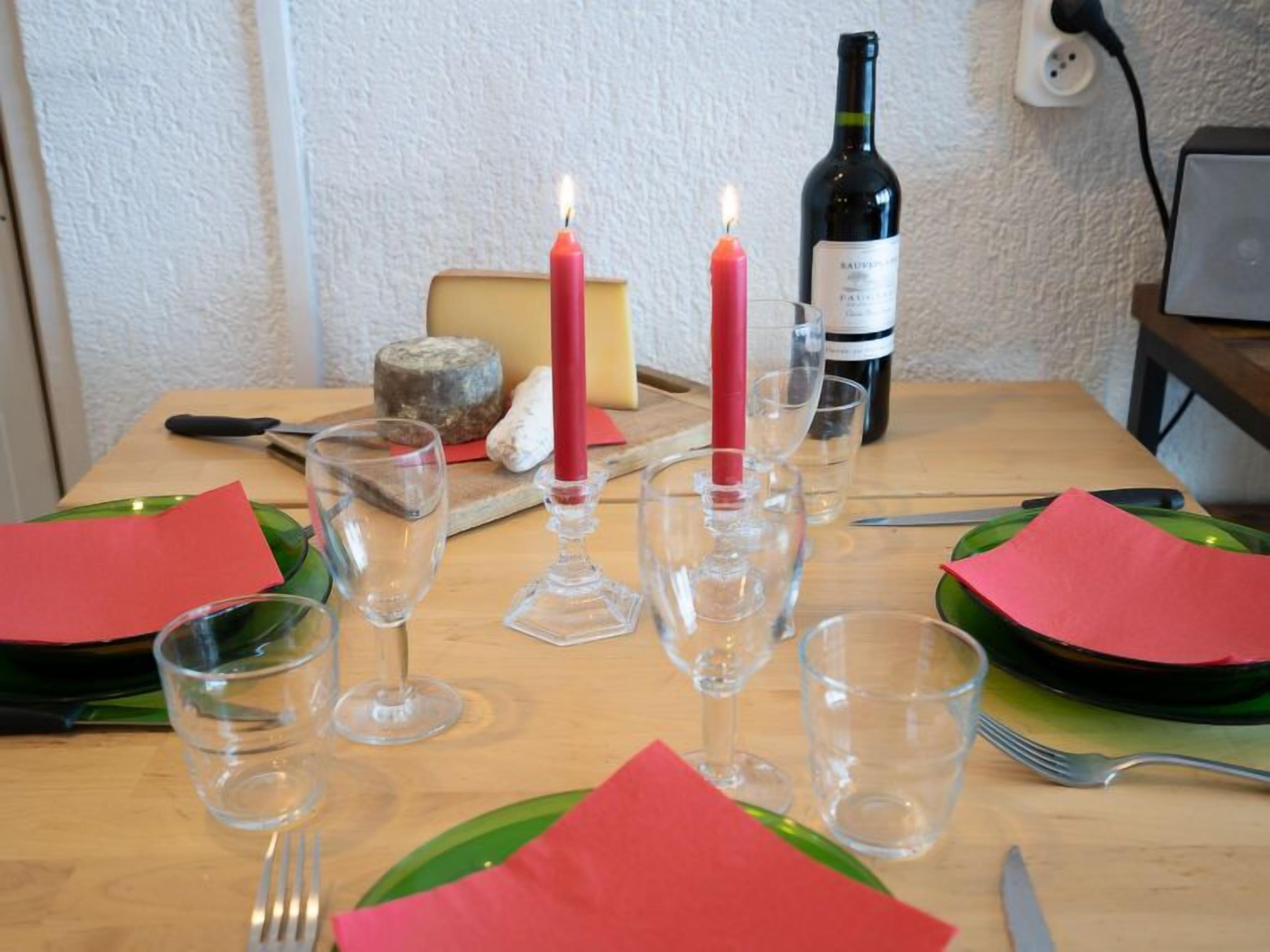 Mesa de comedor con servilletas rojas, copas de vino transparentes y una vela.