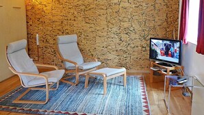 Uma sala de estar com dois poltronas, uma televisão e uma parede estampada.