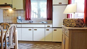 Uma cozinha compacta com armários brancos, um painel de azulejos, uma janela com cortinas vermelhas, uma pia e uma área de refeições com cadeiras de madeira.
