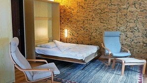 Quarto compacto com cama, duas cadeiras, guarda-roupa e tapete estampado.