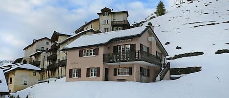A multi-story hotel with balconies, set against a snowy mountain backdrop.
