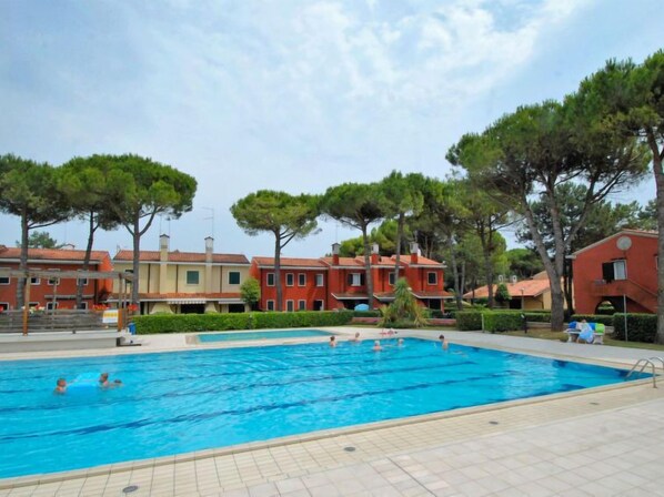 A swimming pool surrounded by buildings with red and beige facades, trees, and a clear sky.