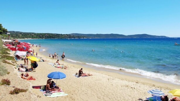 A beach with people sunbathing and swimming, umbrellas, and a clear blue sky. - La Palmeraie by Interhome (Cavalaire)
