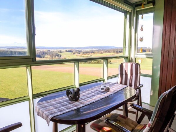 Un invernadero con una mesa, sillas y vistas a un paisaje verde.