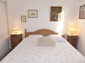 Quarto com cama de madeira, roupa de cama floral, duas mesas de cabeceira com luminárias e quadros nas paredes.