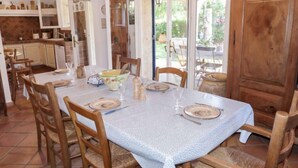 A dining area with a table set for four, surrounded by wooden chairs. A kitchen is visible in the background with cabinets and a countertop. - Le Petit Olivier by Interhome (Les Issambres)