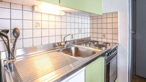 Une cuisine dotée d’un évier en acier inoxydable, de deux plaques de cuisson et d’un dosseret carrelé.