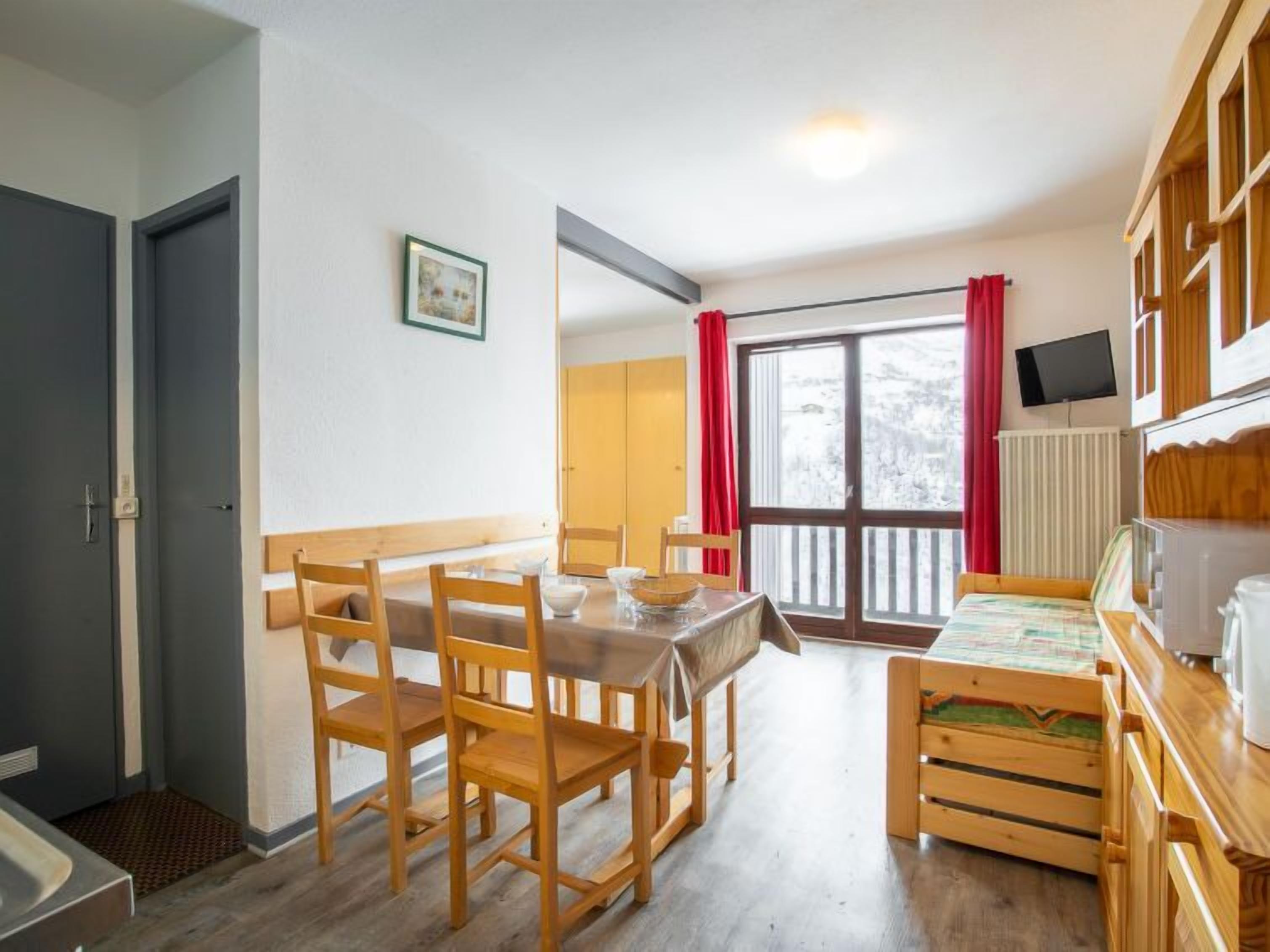 Un comedor con una mesa y sillas de madera, una cocina con estufa y armarios, y un ventanal con cortinas.