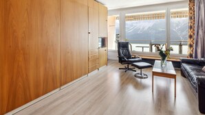A modern living room with wooden cabinets, a black leather chair, a wooden coffee table, and a sofa. - Promenade Apt 210 by Interhome (Arosa)