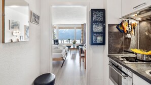 A modern kitchen with a stove, sink, and hanging utensils. A dining area with a table and chairs is visible through an open door. - Promenade Apt 210 by Interhome (Arosa)