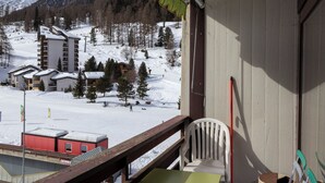 Un balcon offrant une vue sur une région montagneuse enneigée, avec des bâtiments et des arbres.