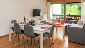 Ein moderner Essbereich mit einem weißen Tisch, gedeckt für vier Personen, grau gepolsterten Stühlen und einem an der Wand montierten Fernseher.