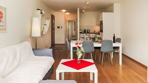 Ein modernes Wohnzimmer mit einem weißen Sofa, einem grauen Sessel und einem Essbereich mit weißem Tisch und roter Unterlage.