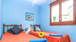 A room with two beds, each with a wooden headboard and orange bedding. There is a framed picture on the wall and a window with wooden shutters.