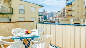 A balcony with a table set for two, white plastic chairs, and a table umbrella.