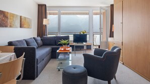 A modern living room with a sofa, armchair, and ottoman, a TV, and a balcony with a view. - Promenade Apt 111 by Interhome (Arosa)