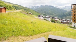 Blick von einer Hügelkuppe auf eine Wohngegend mit modernen Gebäuden, einer Straße und Bergen im Hintergrund.