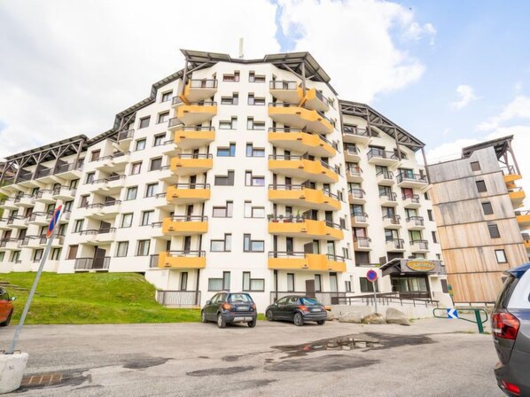 Un immeuble résidentiel à plusieurs étages, doté de balcons, d’un espace de stationnement et d’un petit commerce.