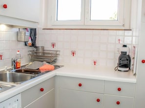 A kitchen with white cabinets, a stainless steel sink, a coffee maker, and a window with white frames.