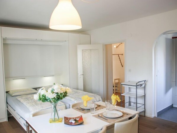 A clean, modern room with a bed, bedside table, and a small dining area.