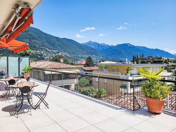 Eine Terrasse mit Gartenmöbeln, einem Blumentopf und Blick auf Berge.