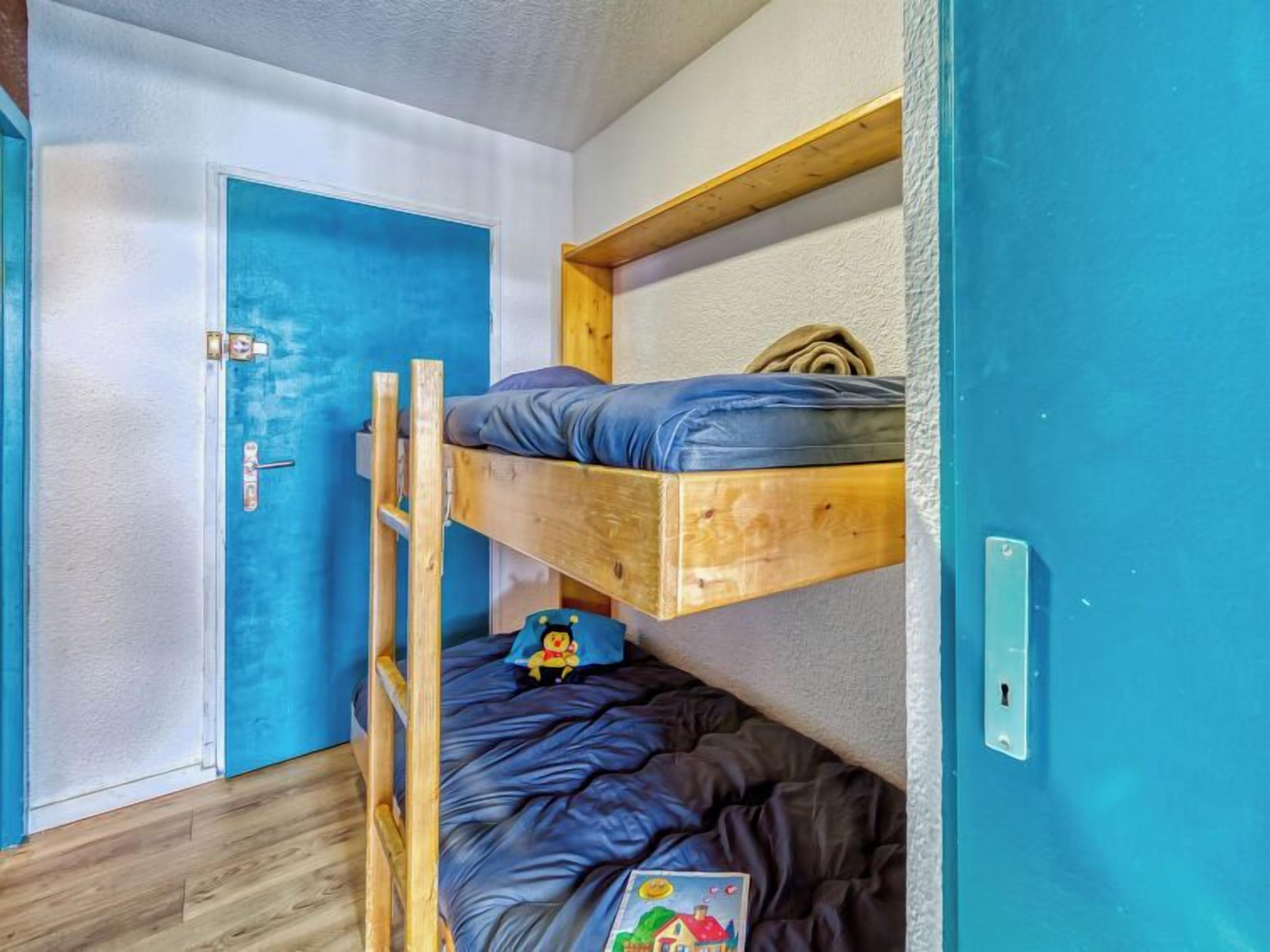 A bunk bed room with a blue door and a wooden ladder.