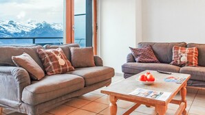 Ein modernes Wohnzimmer mit zwei Sofas, einem Couchtisch und Blick auf schneebedeckte Berge durch große Fenster.