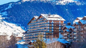 Ein mehrstöckiges Hotel mit Balkonen vor verschneiter Bergkulisse.