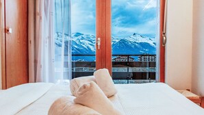 Ein Hotelzimmer mit Bett, Blick auf schneebedeckte Berge und einem Balkon mit Geländer.