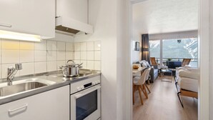 A modern kitchen with white cabinets, stainless steel appliances, and a view of a dining area with a table and chairs. - Promenade Apt 409 by Interhome (Arosa)