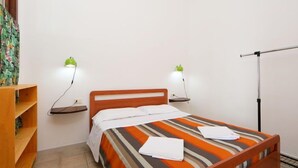 A single bed with a striped bedspread, two bedside tables with lamps, a wooden nightstand, and a radiator. - Limette 2 by Interhome (Valledoria)