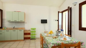 A compact kitchen with a dining table set for two, a TV mounted on the wall, and a window with a view. - Limette 2 by Interhome (Valledoria)