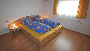 A bedroom with a wooden bed, a nightstand, a window with curtains, and a ceiling light. - Mangeng by Interhome (Schruns)