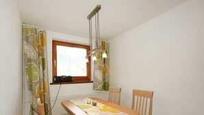 A small dining area with a table and chairs, a window with curtains, and a hanging light fixture. - Mangeng by Interhome (Schruns)
