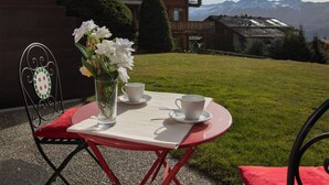 A table with a vase of flowers and two cups, set on a red tablecloth outdoors with a mountain view in the background. - Diure 0113 by Interhome (Verbier)