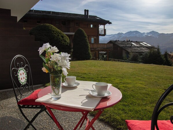 A table with a vase of flowers and two cups, set on a red tablecloth outdoors with a mountain view in the background. - Diure 0113 by Interhome (Verbier)