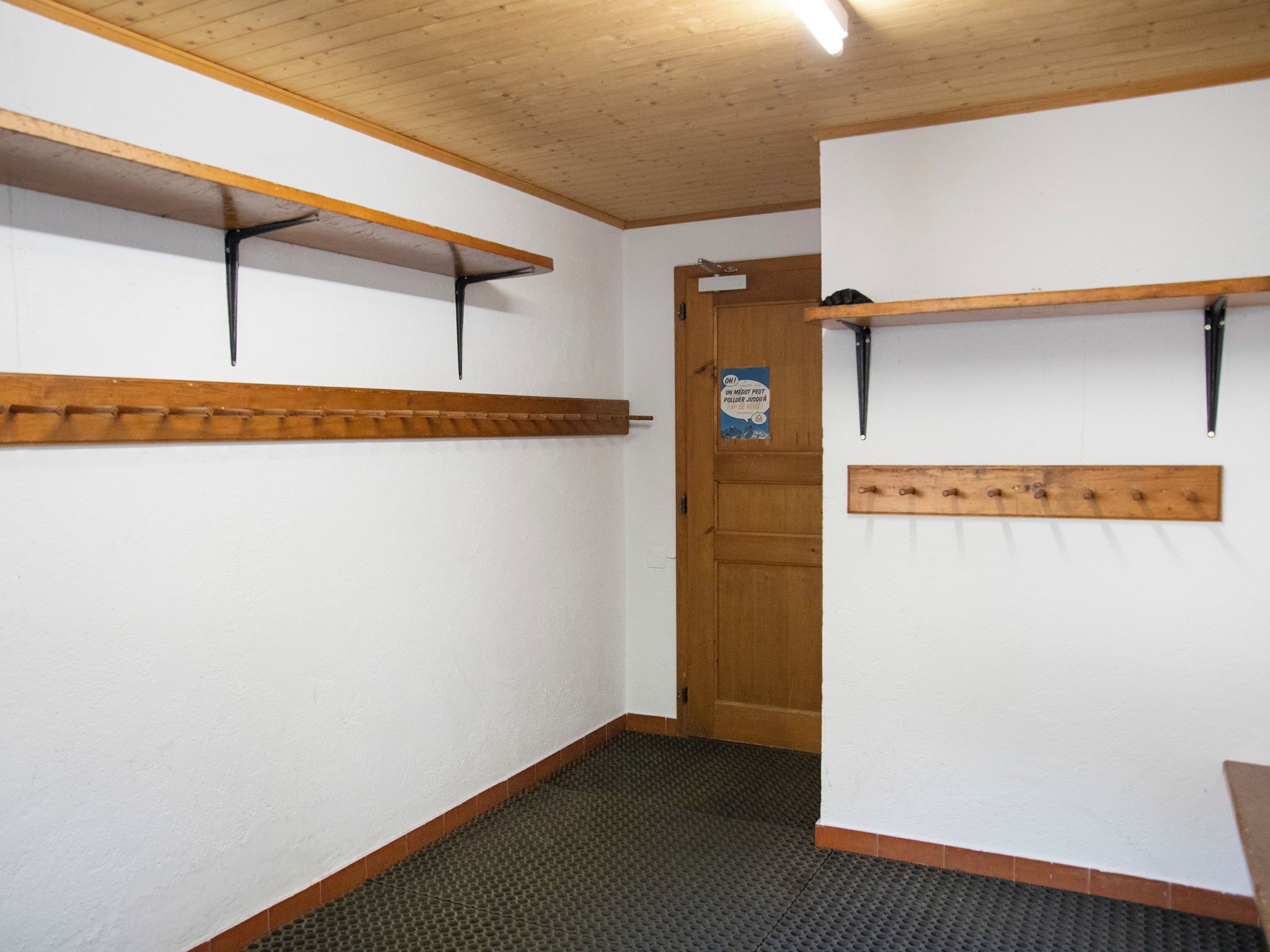 A hallway with wooden shelves, a door with a sign, and a textured floor.
