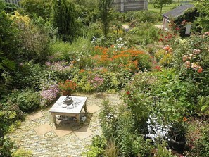 A garden with a stone table and a teapot, surrounded by various plants and flowers.